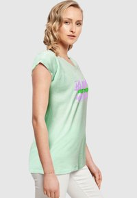 Mørkegrøn bomulds t-shirt med korte, rullede ærmer, der har et iøjnefaldende pink og grønt grafisk tekstdesign på forsiden. Figursyet silhuet.