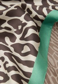 Tissu soyeux avec un motif animalier marron et beige, bordé d'un bord lisse vert sarcelle, montrant des plis et des détails de texture.