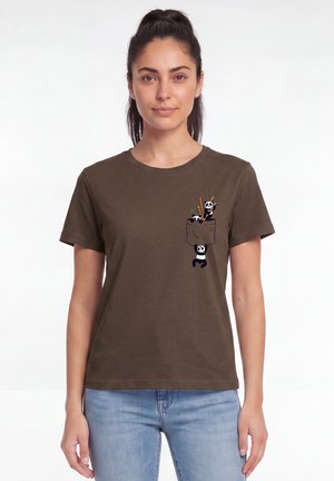 Femme portant un t-shirt marron avec des pandas dessinés grimpant et assis dans une poche imprimée sur la poitrine gauche, associé à un jean bleu clair.