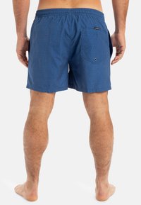 Modré plavky s textúrovaným vzorom, elastický pás, bočné vrecká a zadné vrecko s detailom gombíka.