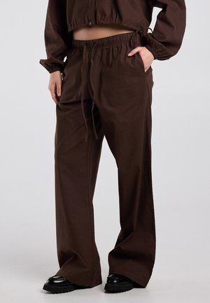 Person wearing dark brown wide-leg pants with elastic waistband and drawstring, paired with black chunky shoes on gray background.