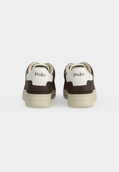 Καφέ και λευκά sneakers Polo, ορατά από πίσω, με εκρού σόλες και λογότυπο «Polo» στην ταμπέλα της φτέρνας, σε μονόχρωμο φόντο.