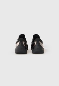 Pár čiernych a kovových slip-on sneakers s pohľadom zozadu na jednoduchom bielom pozadí.