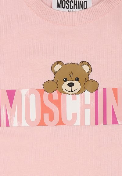 T-shirt en coton rose avec un graphique d'ours brun jetant un œil au-dessus du mot "MOSCHINO", accompagné d'une écriture en gras et multicolore en dessous de l'ours.