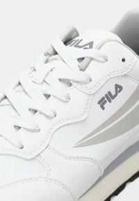 White leather sneaker with grey accents, featuring a smooth texture, rounded design, and prominent laces. Logo displayed on the side.
