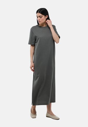 Robe grise, longueur genou, à manches courtes en tissu doux avec une coupe décontractée et des fentes sur les côtés, portée avec des chaussures plates neutres.
