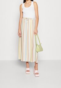 Kvinde iført en hvid top, pastelfarvet, vertikalt stribet midi-nederdel, lyserøde plateau-sandaler, mens hun holder en lille lysegrøn håndtaske.