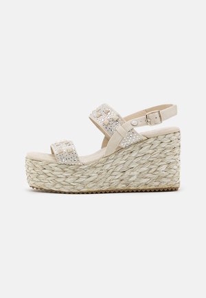 Beige kilehæl sandal med flettet platformsål, to stropper med nitter, en ankelrem med spænde og en gummi ydersål med struktur.
