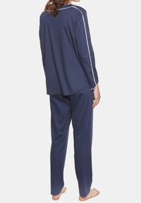 Navy-Pyjama-Set mit einem Langarmoberteil mit weißen Paspeln und passenden, locker sitzenden Hosen. Weicher Stoff, entspannte Passform. Barfuß sichtbar.