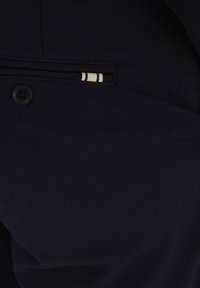 Crni materijal s glatkom teksturom ima džep s uzorak podstavom u bež i krem horizontalnim prugama, a detalj s crnim gumbom.