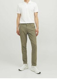 Polo shirt bianco leggero a maniche corte abbinato a pantaloni slim-fit verde oliva e scarpe sportive bianche, in piedi su uno sfondo neutro.