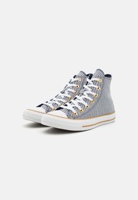 Zapatillas altas con tela a rayas en azul marino y blanco, suela de goma blanca, ojales dorados y cordones blancos. Diseño minimalista con acentos contrastantes.