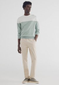 Helles blauer und grauer Pullover mit Rundhalsausschnitt, langen Ärmeln und gerippten Bündchen, kombiniert mit beigen Hosen und grauen legeren Schuhen.