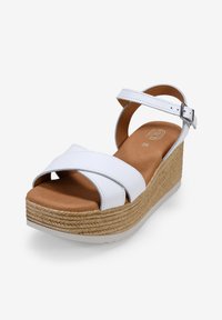 Sandalias de cuña blancas de cuero con correas entrelazadas, suela tipo corcho y una plantilla suave marrón. Se ajustan con una hebilla plateada.