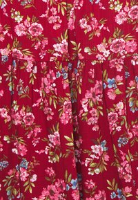 Tela floral roja con flores rosas y azules y hojas verdes, texturizada con sutiles pliegues, creando un patrón vibrante.