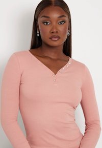 Rožinė ilgaaijonė megztinė su V formos iškirpte ir dekoratyviniais mygtukais ant peties. Lygus paviršius ir prigludusi forma suteikia elegantišką išvaizdą.