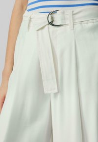 Witte broek met een brede, geplooide vormgeving. Beschikt over een riem met een ronde zilveren gesp en een gladde textuur.