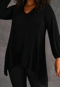 Top negro de manga larga con escote en forma de V, confeccionado en un material suave y brillante; presenta un dobladillo asimétrico y mangas fruncidas.