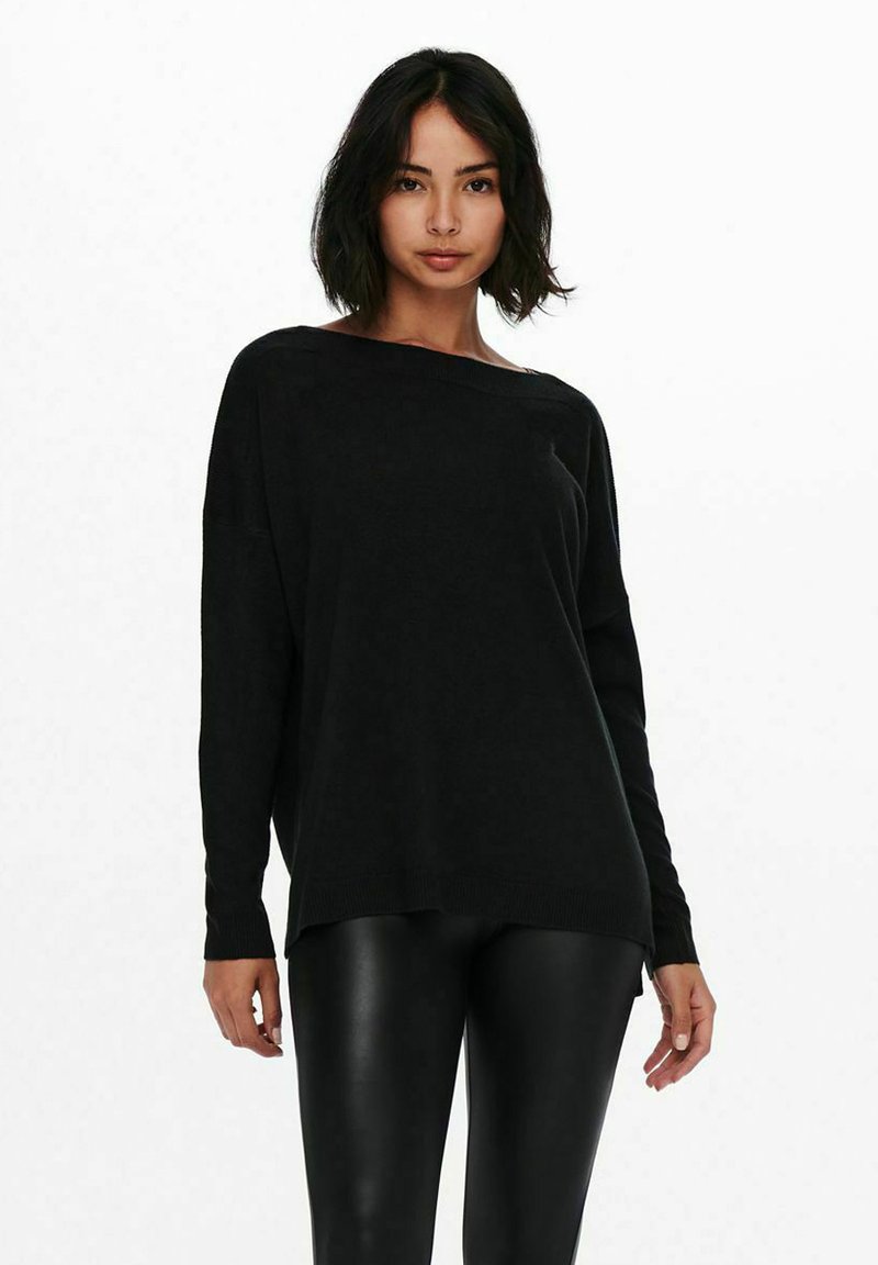 Pull en tricot noir avec une coupe ample et un large col, doté de manches longues et de poignets côtelés. Associé à un legging noir ajusté.