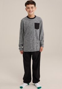 Siva dolgi rokav s črno žepom, v kombinaciji s črnimi hlačami. Udobna, sproščena oblačila za prosti čas, z rebrastimi manšetami in nogavicami z zelenimi poudarki.