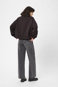Felpa cropped marrone scuro e jeans a gamba larga grigi. La felpa presenta una vestibilità morbida e polsini a costine. Calzature nere completano l'outfit.