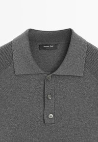 Szara koszulka polo o miękkiej teksturze, z kołnierzykiem, trzema guzikami na plisie i prążkowanymi akcentami na szwach ramion. Widoczna metka marki.