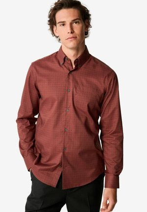 Chemise à manches longues à motifs rouges avec un col boutonné et des boutons foncés, présentant une coupe ajustée et une texture lisse.