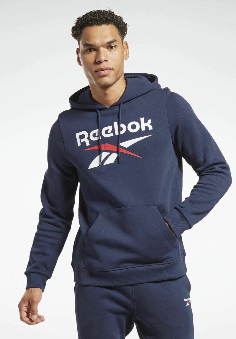 Marineblå Reebok hoodie lavet af blødt stof med en frontlomme, der har et stort hvidt og rødt logo på brystet samt hætte med snøring.