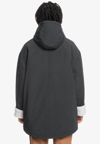 Tmavo �šedá nadmerná bunda s kapucňou, so zamatovými bielymi kožušinovými manžetami a hladkým, mierne lesklým povrchom. Jednoduchý, štruktúrovaný dizajn.