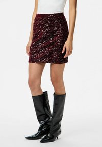 Mini falda de lentejuelas burdeos con cintura ajustada y superficie texturizada. Combinada con botas negras de charol por encima de la rodilla con punta afilada.