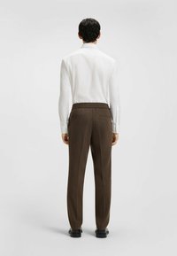 Bruine op maat gemaakte broeken met een gestructureerde afwerking, elastische tailleband en zijzakken, gecombineerd met een witte overhemd met lange mouwen.