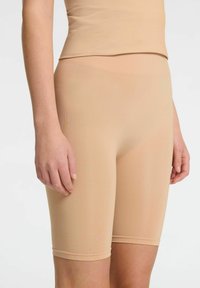Beige strækshorts med en tætsiddende design, glat overflade og længde til midt på låret. Har en sømløs talje og blød stoffinish.