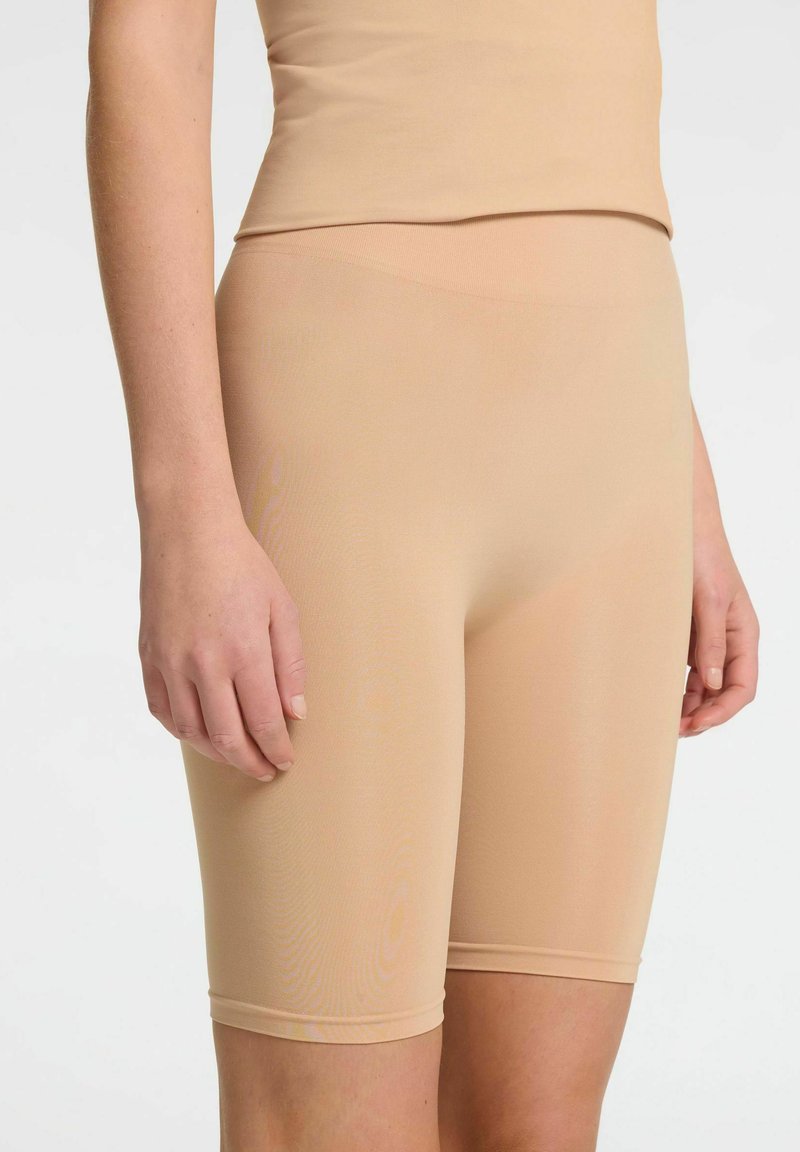 Beige strækshorts med en tætsiddende design, glat overflade og længde til midt på låret. Har en sømløs talje og blød stoffinish.