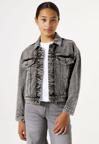 Spijkerjas in vervaagd zwart met een klassieke snit, voorzakken, knoopsluiting en een licht versleten textuur, gecombineerd met grijze jeans.
