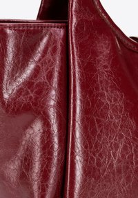 Bordeaux leren boodschappentas met een gladde, glanzende afwerking. Heeft een geplisseerde textuur en stiksels langs de naden. Geen zichtbare hardware accenten.