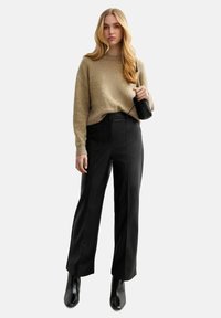 Maglione beige a trama, pantaloni neri a vita alta, stivaletti neri con punta e una piccola borsa nera. Outfit semplice ed elegante.