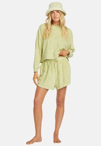 Svetlo zelena loungewear dolgovratna kombinacija iz frotir materiala, ki vključuje krajšani pulover z vzorci listov in usklajene kratke hlače z nastavljivim vrvico.