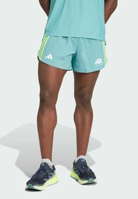 Aqua shorts med neongröna accenter och tre vita ränder, ihop med marinblå löparskor med en ljusgul sula och grå detaljer.