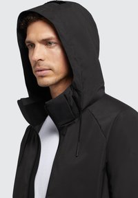 Giacca leggera nera con colletto alto e cappuccio regolabile. Presenta una texture liscia e una cerniera frontale di contrasto.
