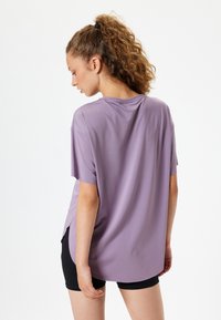 Løst siddende t-shirt med korte ærmer i lavendelstof med en glat overflade; har sidedrage og en rund halsudskæring.