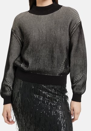 Kvinde iført en sort og sølvstribet langærmet sweater kombineret med et sort palietnederdel med frynse detaljer.