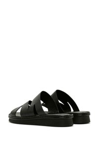 Sandali in pelle nera con ampi cinturini a taglio e suola texturizzata. Design piatto con dettagli cuciti e una finitura liscia.