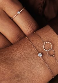 Roze gouden armbanden op een hand hebben een kleine ronde diamanten accent en onderling verbonden ringen, die een verfijnd kettingontwerp en textuur laten zien.