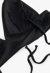Top bikini nero a forma triangolare, realizzato in tessuto morbido. Presenta spalline regolabili e un dettaglio di bordatura cucito.
