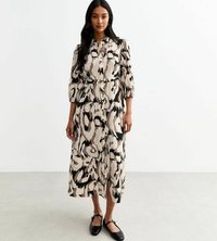 Langes, knopfbares Kleid in einem beigen und schwarzen abstrakten Muster. Hat gepuffte Ärmel, eine taillierte Taille und eine Midi-Länge. Schwarze flache Schuhe.