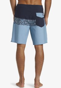 Shorts de bain pour hommes en bleu et marine, avec un motif géométrique, en tissu léger, taille élastique et une poche arrière avec fermeture à bouton.