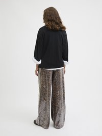 Black long-sleeve top with white cuffs, paired with wide-leg pants featuring a sequined animal print in earthy tones and a smooth texture.