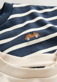 Tela a rayas azul y blanca con un pequeño coche naranja bordado, parcialmente cubierto por un cuello de tela ribeteada beige.