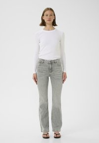 Bílý dlouhý rukáv ribbed top v kombinaci s světle šedými zvonovými džíny. Džíny mají klasický design s pěti kapsami a jemné vyblednutí. Černé žabky.