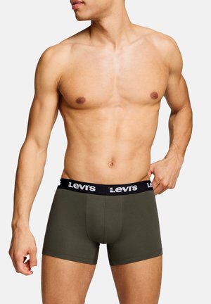 Muskelöser männlicher Oberkörper trägt olivgrüne Levi's Boxershorts mit schwarzem Bund, Hand passt den Bund auf der rechten Seite an.